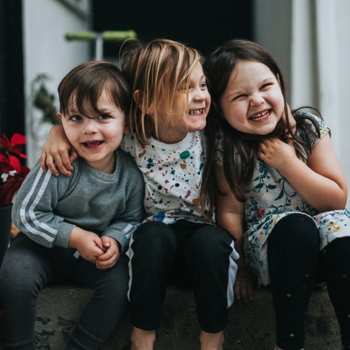 A boy and two girls sitting outside and smiling